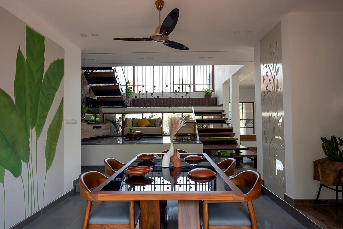 Dining area with a cut-out jaali screen and vertical wooden louvres looking into the living room of a Kerala home