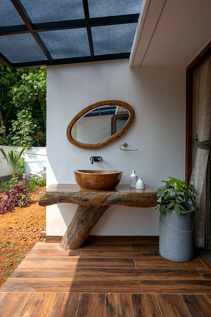 Semi-open wash area with a wooden basin under a glass roof, opening to the garden of a Kerala home