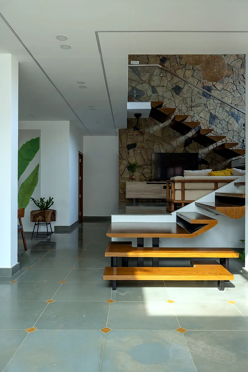 Natural stone wall with a floating wooden staircase and grey stone flooring in a modern tropical house in Kerala