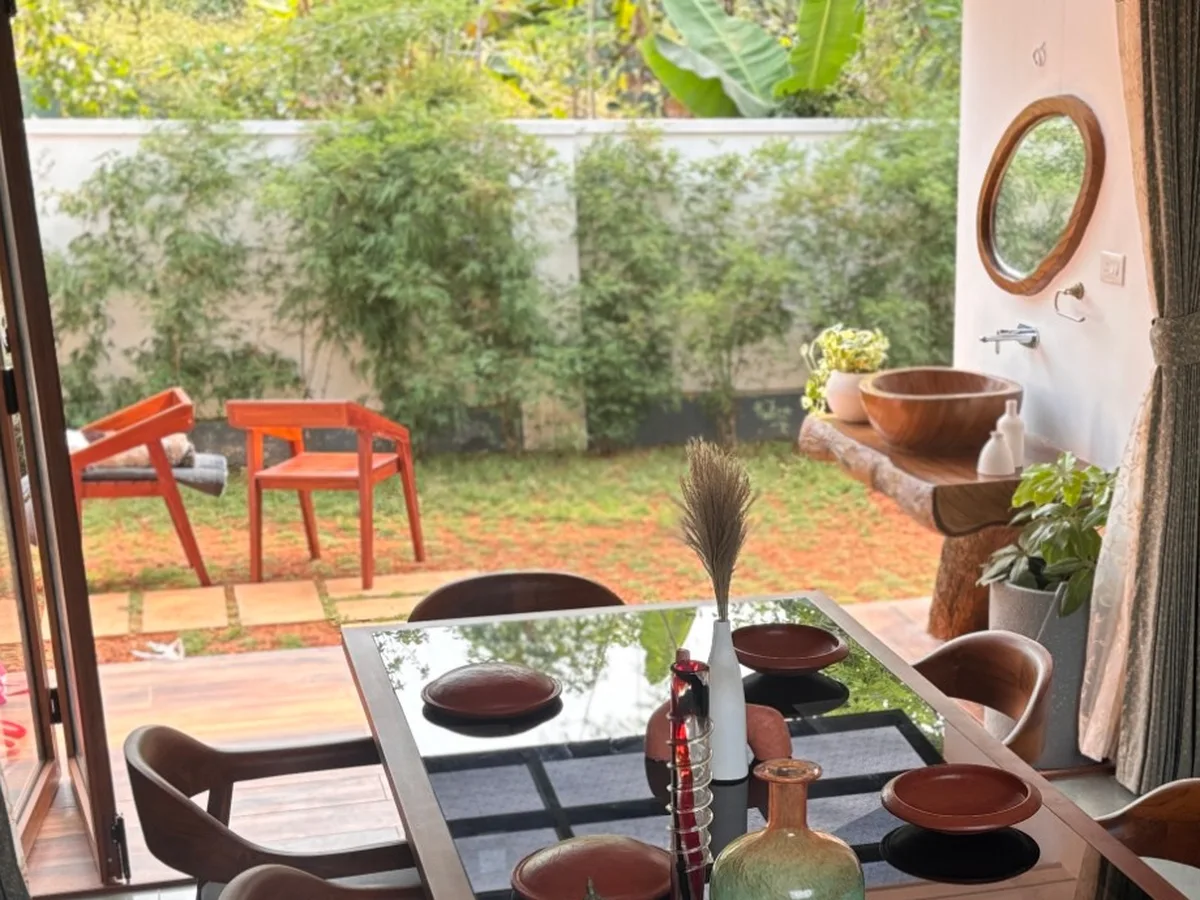 Dining room with a wooden table and chairs opening through folding doors to a garden, with a painted leaf mural on the wall